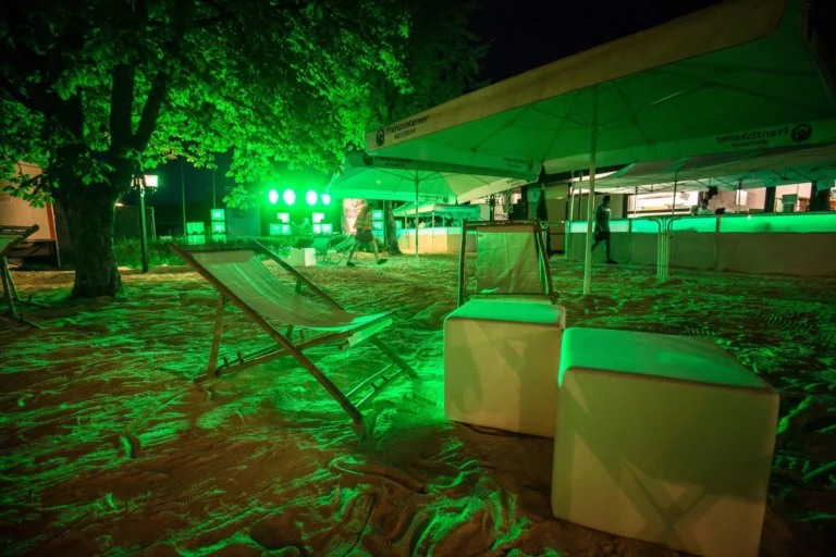 Sitzwürfel, Liegestühle und ein überdachter Stand im grün beleuchteten Außenbereich der Beachparty Gundelfingen.