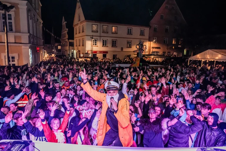 Viele kostümierte Besucher stehen bei Nacht vor der beleuchteten Bühne auf dem Platz zwischen historischen Häusern in Weißenhorn.