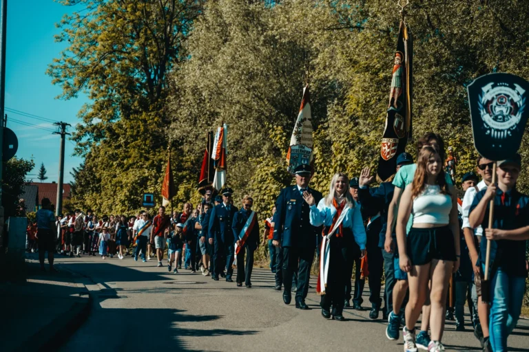 Eine lange Reihe von Teilnehmern geht mit Vereinsfahnen und Schildern auf einer Straße unter Bäumen beim Jubiläum des TSV Wasserburg.