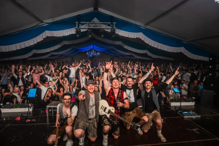 Die Band kniet und steht am Bühnenrand mit Instrumenten vor dem dicht gefüllten Festzeltpublikum mit erhobenen Händen.