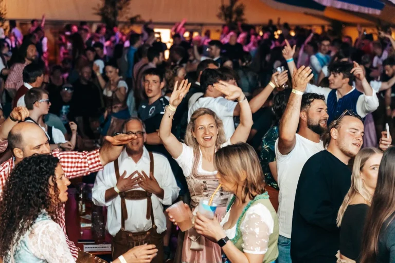 Gäste in Dirndln und Hemden heben Hände und Becher auf der dicht besuchten Tanzfläche im Festzelt.
